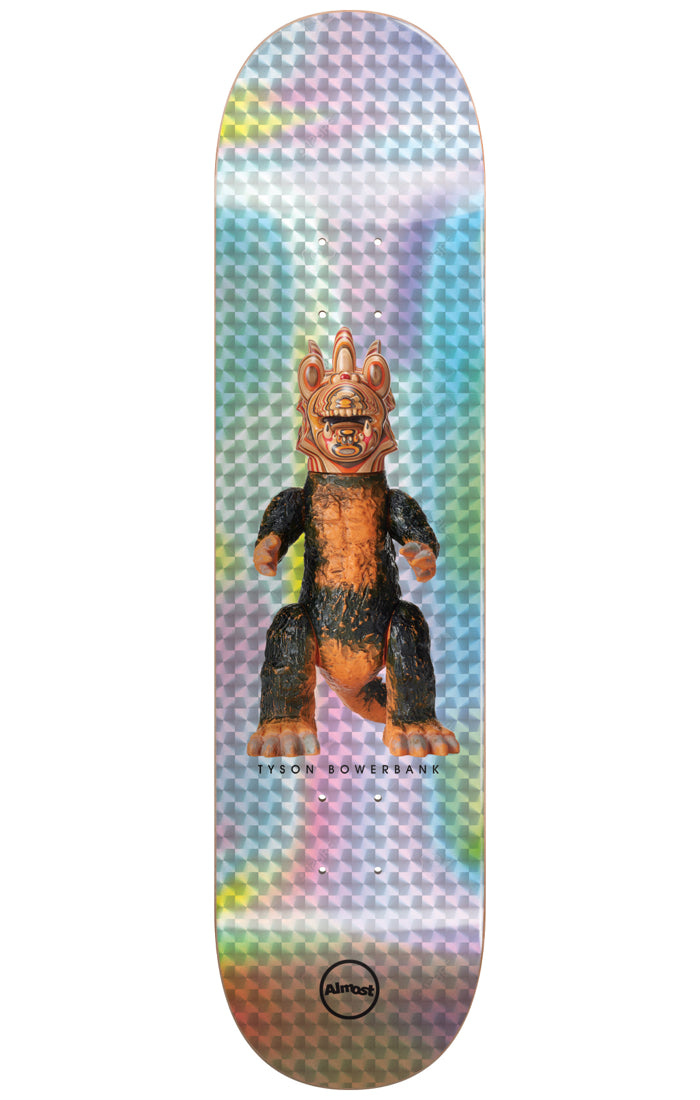 Almost Bowerbank Haroshi Monster Super Sap R7 8.0 & 8.25 skateboard deck: A vinyl toy-style monster with a crested orange head and black and orange furry body stands centred on a holographic silver foil background with a faceted pattern. The rider's name is printed beneath it and the Almost circle logo sits at the tail.