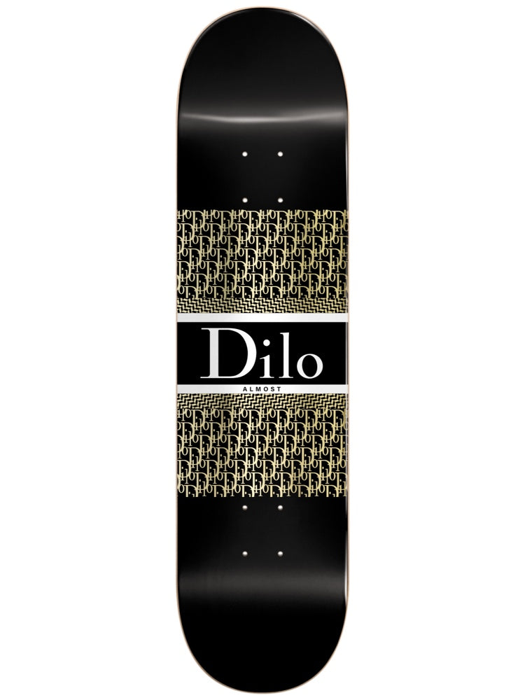 Almost Dilo Luxury Super Sap R7 8.125 skateboard deck: Black deck with a luxury fashion-label parody: a white-bordered black panel with serif "Dilo" in white, between two bands of repeating gold monogram lettering.