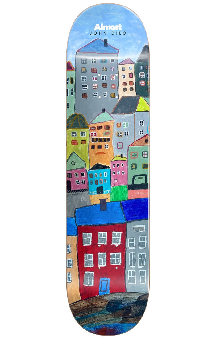 Almost Dilo Places R7 LEFT 8.125 skateboard deck: Naive painted townscape of colourful houses stacked up a hillside, with tiny windows, against a blue sky. A red house with a blue door sits in the foreground. Almost logo and John Dilo name at the top.