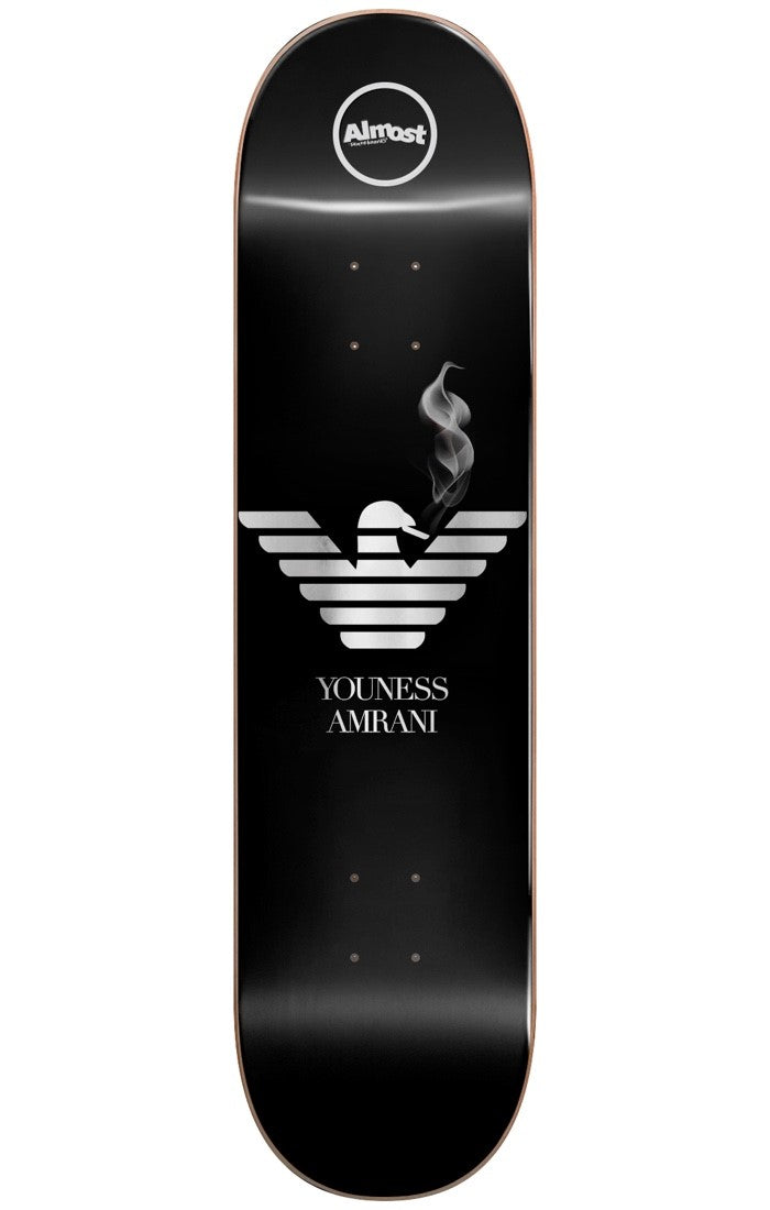 Almost Youness Runway R7 8.25 skateboard deck: Black deck with a silver striped eagle emblem in the manner of a fashion label logo, a wisp of smoke rising from its head. The rider name is in serif capitals beneath, with the round Almost logo at the nose.