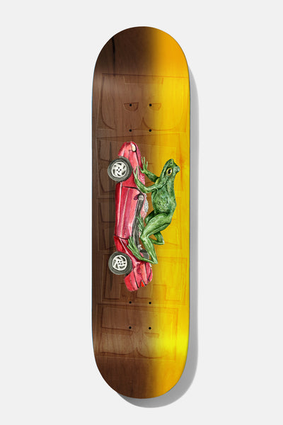 Baker Figgy Dimensions 8.5 skateboard deck: Wood-stained deck fading from brown to yellow-orange, with a faint ghosted Baker logo and a painted green frog pushing a red car along on its side.