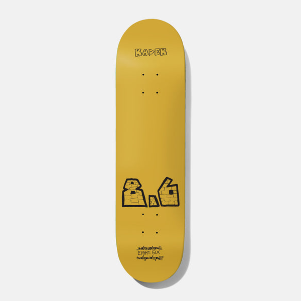 Baker Spanky Mega 8.625 skateboard deck: A plain mustard-yellow deck with the name Kader in small black hand-drawn capitals at the top. Near the tail is a large brick-textured 8.6 in thick black outline, with EIGHT SIX written between barbed-wire scribbles.