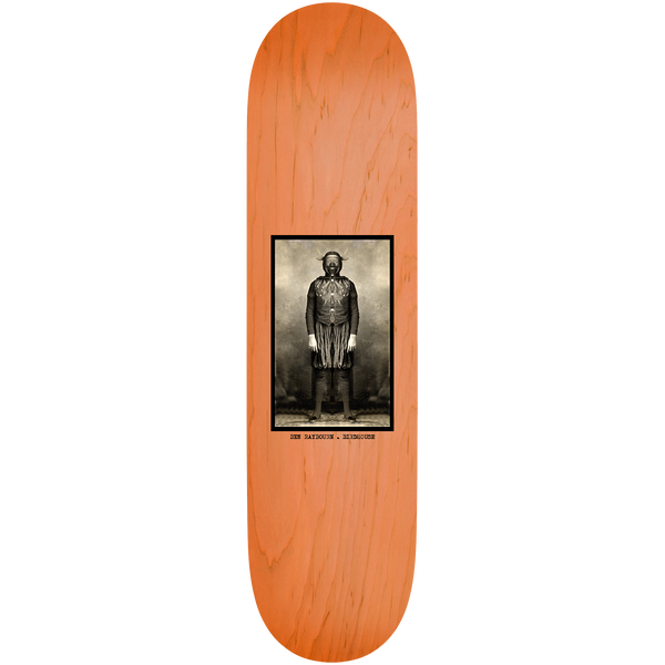 Birdhouse Ben Raybourne Beautiful Mutants 8.38 skateboard deck: A small framed sepia photograph of a standing figure in a costume with horned mask and fringed skirt, centred on an orange-stained wood deck, with a typewritten caption beneath.