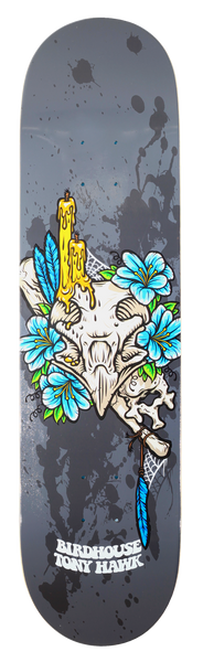 Birdhouse Tony Hawk Shrine skateboard deck: An animal skull topped with dripping yellow candles, ringed with blue flowers, a bone, a blue feather and cobweb, on a grey background with black paint splatters.