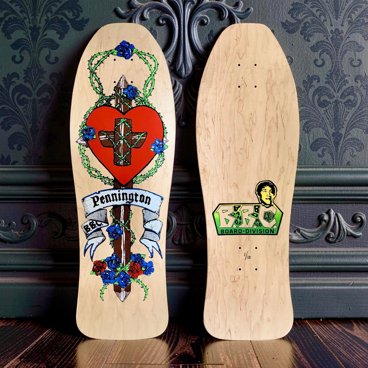 Brand-X Bryan Pennington Crucifix skateboard deck: Old-school shaped deck on natural wood showing a red heart with a wooden cross wrapped in thorny vines, set on a spiked post with blue and red roses and a ribbon banner. Underside has a green and yellow board logo with a cartoon face.
