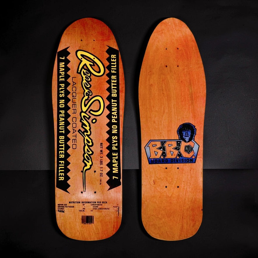 Brand-X Reese Simpson Buttercup skateboard deck: Old-school shape on orange stain styled as a peanut butter jar label: yellow script Reese Simpson name, black zigzag-edged panels reading 7 maple plys no peanut butter filler, nutrition panel and barcode. The underside shows a B.B.C. Board Division logo with a portrait.