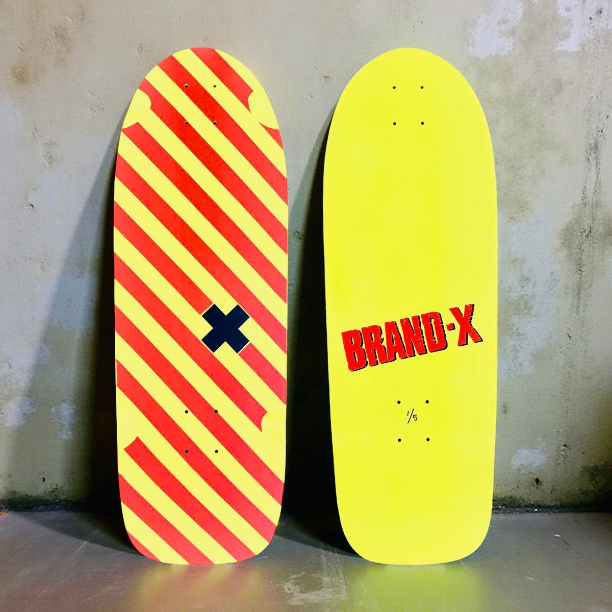 Brand-X Vertical Hold skateboard deck: Old-school shaped yellow deck with diagonal red stripes and a small navy cross in the middle; the underside is plain yellow with red BRAND-X lettering and 1/5 edition mark.