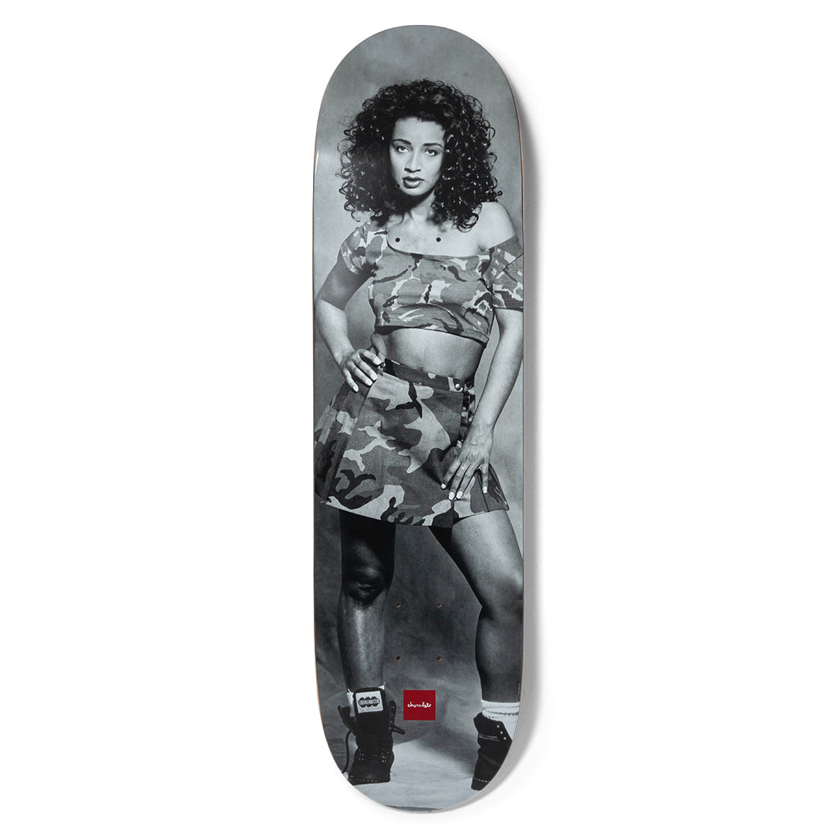 Chocolate Aikens Disco Toni Pop Secret skateboard deck: A black and white photo of a woman with curly dark hair posing with hands on hips in a camouflage crop top and skirt, with high-top trainers. A small red Chocolate logo sits near the bottom.
