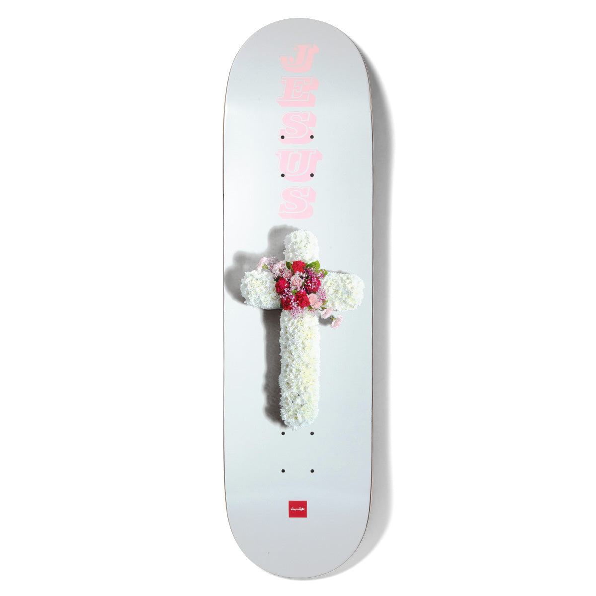 Chocolate Fernandez Flower Cross skateboard deck: A photographed funeral-style floral cross of white carnations with a red and pink flower centre on a pale grey deck. The word JESUS is stacked vertically in pink above it, with a small red Chocolate logo at the tail.