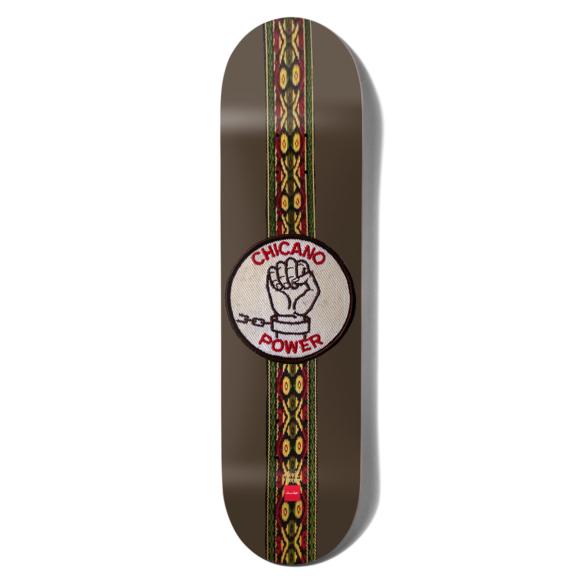 Chocolate Perez Chicano Power skateboard deck: Brown deck with a woven textile stripe in red, yellow and green running its length, and a round embroidered-style patch with a raised fist breaking a chain and the words Chicano Power.