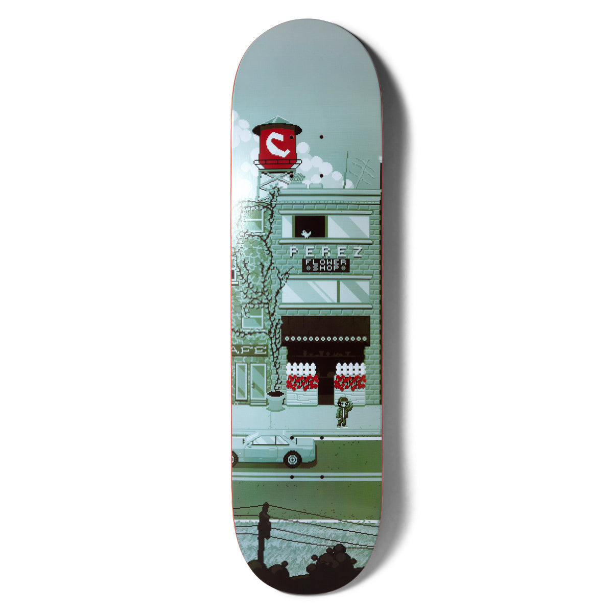 Chocolate Perez Pixel City skateboard deck: Pixel-art street scene in muted greens and grey showing a brick shop front labelled as a flower shop, with a red water tower carrying the Chocolate logo above. A small figure stands outside, with a car and power lines below.