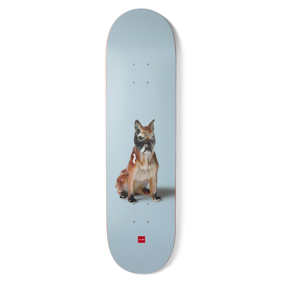 Chocolate Perez Porcelain skateboard deck: Photograph of a glazed porcelain boxer dog figurine sitting on a plain pale blue background, with a small red Chocolate logo at the tail.