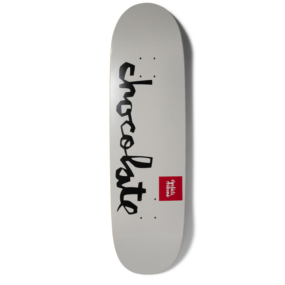 Chocolate Aikens OG Chunk Loveseat+ skateboard deck: Plain light grey wide-nosed deck with the large black brush-script Chocolate logo running down the length, plus a small red square name label to the right.