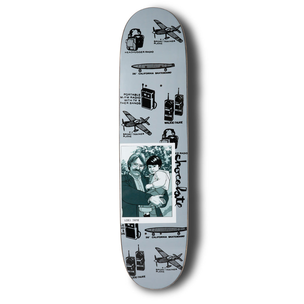 Chocolate York Kid Portrait skateboard deck: Grey deck covered in black line illustrations of headphone radios, walkie-talkies, aeroplanes and a 26-inch California skateboard, with a captioned photo of a man holding a child and a vertical Chocolate logo.
