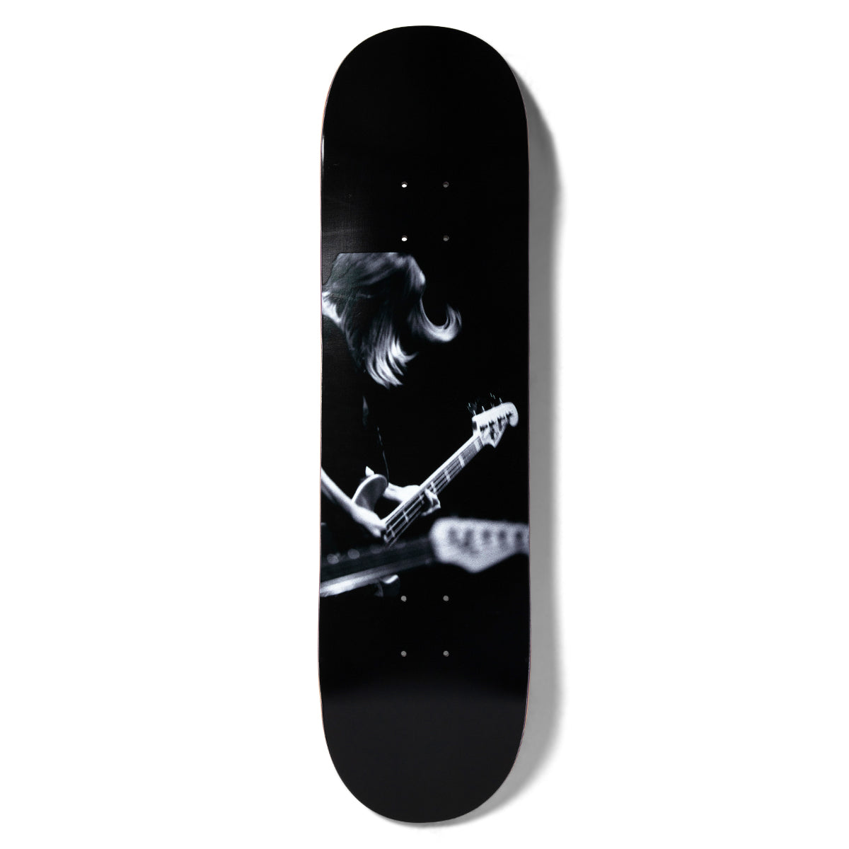 Girl Spike Photo Kim Gordon skateboard deck: A black and white live-music photograph of a long-haired musician bent over a bass guitar, with another guitar neck blurred in the foreground. Dark, moody image on a black deck.