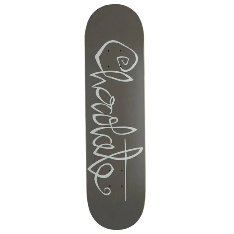 Chocolate Trahan OG Script skateboard deck: Looping, handwritten-style brand script in pale grey running down the length of a plain dark grey deck, with a long underline stroke through the final letters.