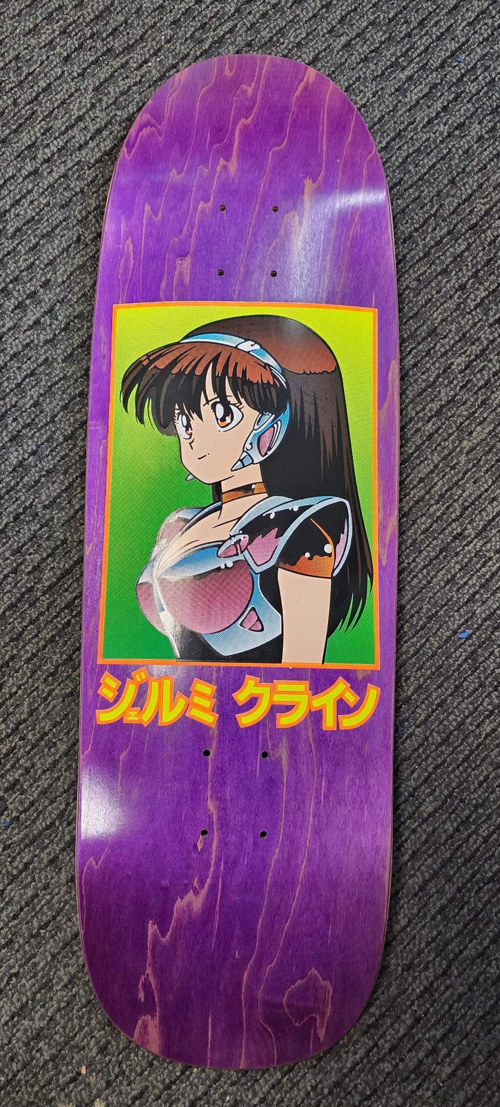 JK Industries Dream Girl Purple skateboard deck: An anime-style girl with long dark hair, headband and metallic armour, framed in a green rectangle with an orange border on a purple stained deck. Japanese katakana text beneath in yellow.