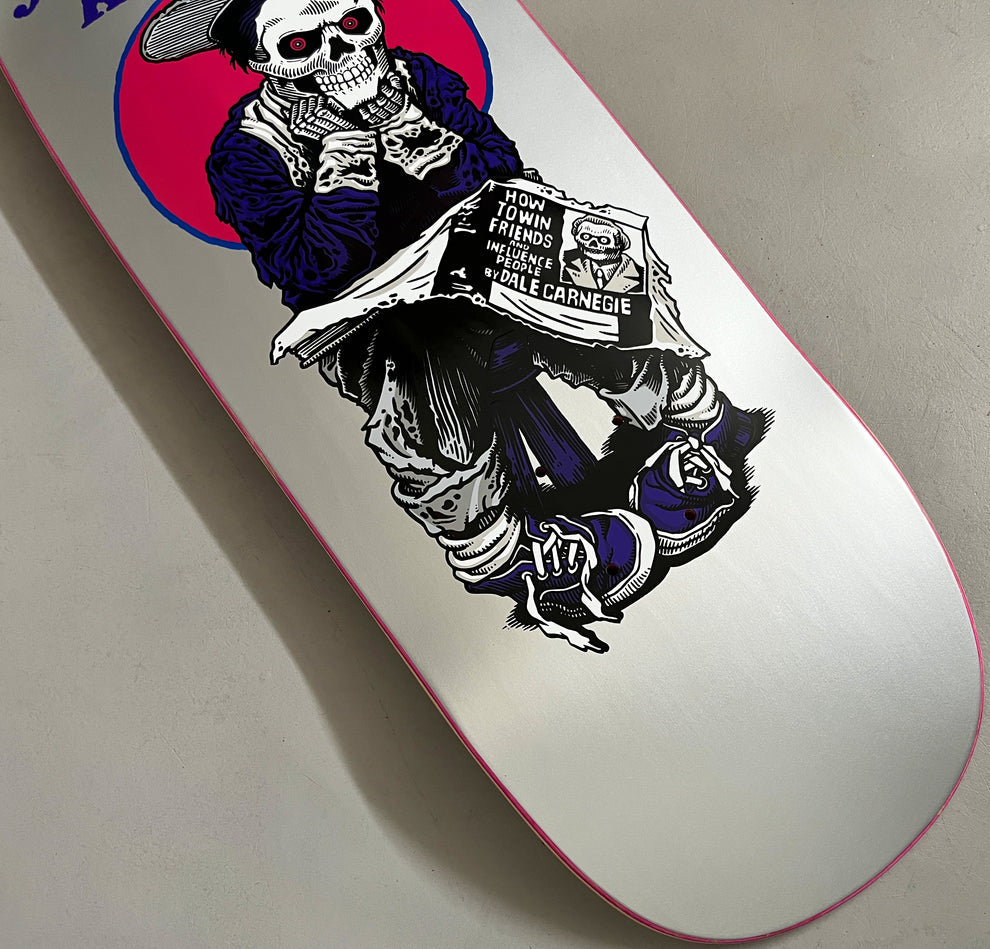 Hook-Ups Jk Industries Jeremy Klein black eye kid skull Metallic Silver skateboard deck: Skeleton newsboy in a cap and purple clothes, seated and reading a newspaper headed How to Win Friends and Influence People by Dale Carnegie, in front of a pink circle, on a metallic silver deck with pink edge. Photo is a partial close-up.