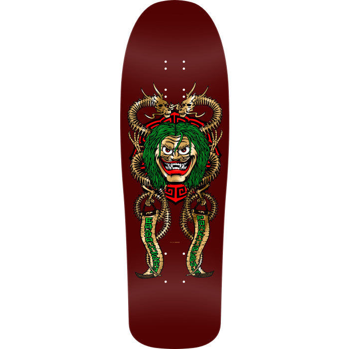 Powell Peralta Caballero Mask Burgundy skateboard deck: A grinning demon mask with green hair and fangs sits over a red geometric emblem, flanked by two gold bone-dragon snakes holding banners with green lettering, on a burgundy old school shaped deck.