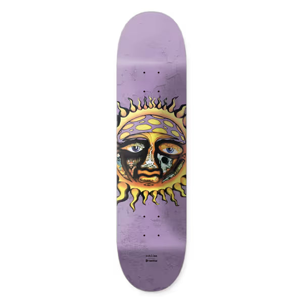 Primitive x Sublime Rise skateboard deck: The Sublime sun face logo in yellow and orange, with eyes, one holding a skull, and small symbols within the features, on a mottled lilac deck. Small Sublime and Primitive text beneath.