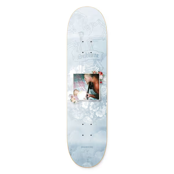 Primitive x Sublime Rythm skateboard deck: A pale blue-grey cloudy background with faint cross outlines and a gothic Sublime banner. A framed colour photo of a shirtless man with a baby in the centre is surrounded by small flowers.