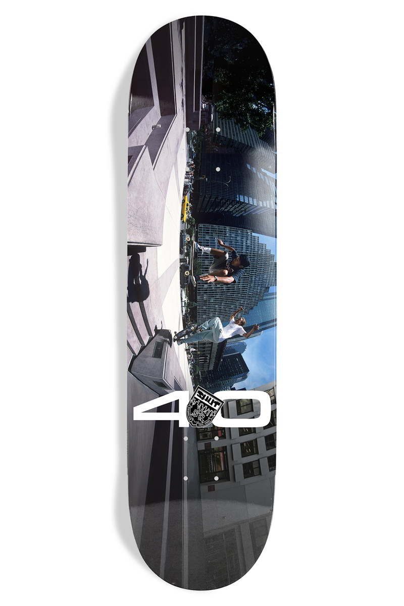 Shut Bryce Kanights Coco & Sheffy EX7 skateboard deck: Full-deck colour photo of two skaters mid-trick between city buildings, shot with a distorted fisheye view and tilted along the deck, with a large white '40' and small crest at the bottom.