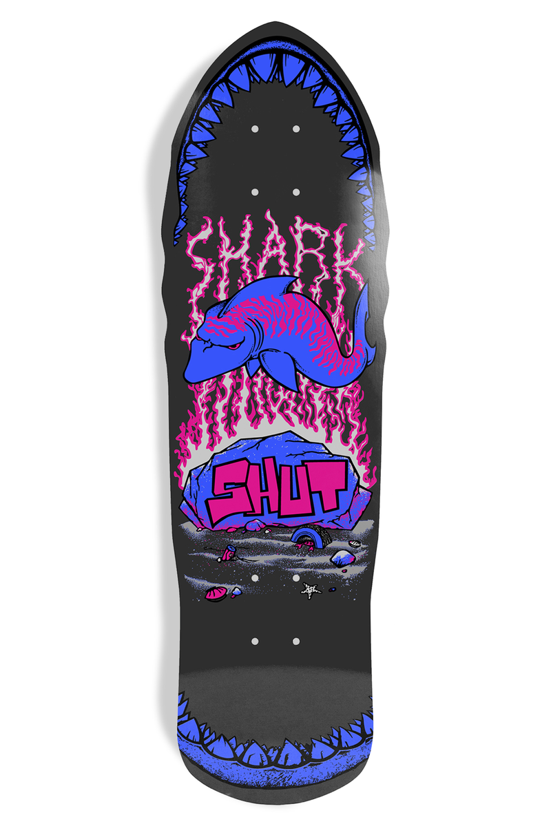 Shut Speed Shark EX7 skateboard deck: Old-school shaped black deck with blue shark-tooth jaws at nose and tail. A pink and blue shark leaps above a rock painted with SHUT, under SHARK in pink lightning-style lettering.