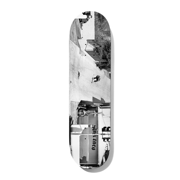 Deathwish Kirby Uncrossed 8.475 skateboard deck: Black and white photograph, turned sideways across the deck, of a skater dropping down a long sloped wall beside a building with a shop sign and a figure with a guitar.