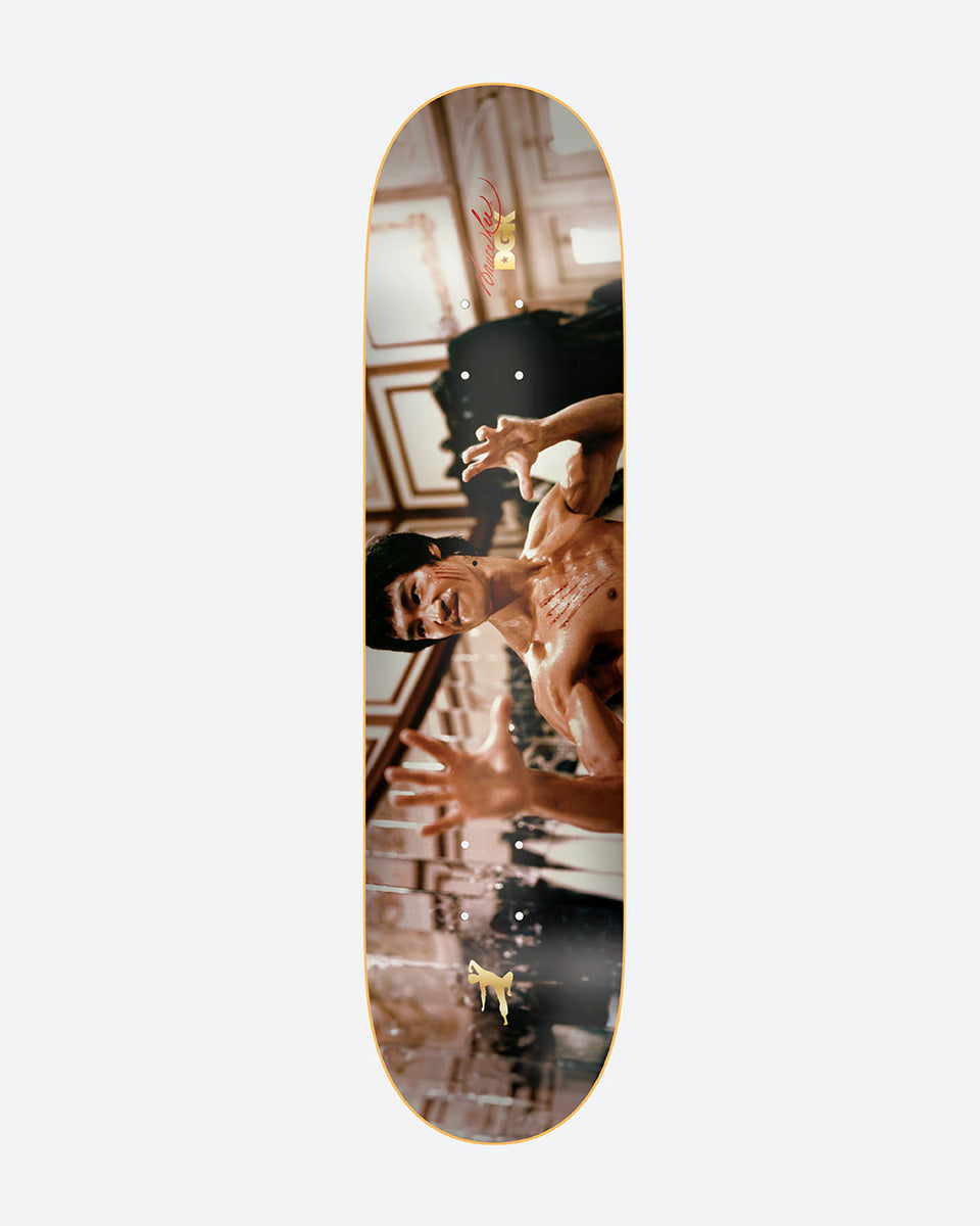 DGK x Bruce Lee Focus skateboard deck: Photographic graphic of a shirtless martial artist in a fighting pose with outstretched hands, in an ornate panelled interior. A red signature and small DGK logo sit near the nose, with a small gold figure at the tail.