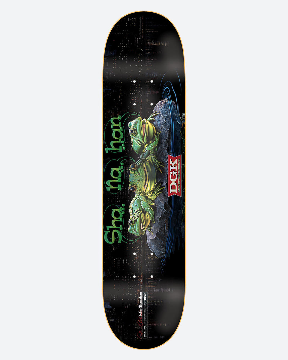 DGK Triplets Shanahan skateboard deck: Painted illustration of three green frogs sitting together on a rock in dark water, with the rider name spelled out in green wavy lettering down the left and a red DGK logo on the right, on a dark black background.