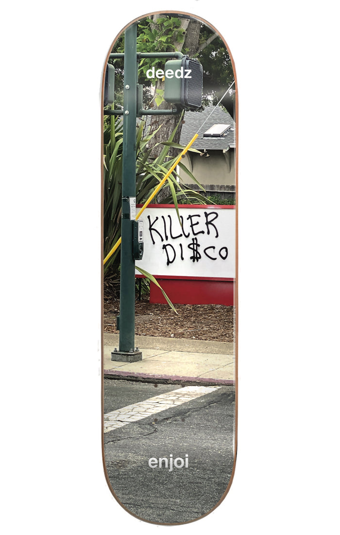 Enjoi Deedz Tweaker R7 8.375 & 8.5 skateboard deck: Full-deck photograph of a street corner with a pedestrian crossing pole and a white sign with graffiti reading Killer Disco, with palm-like plants behind. Rider and brand names in small white text.