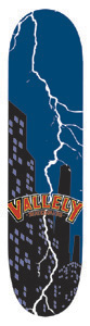 Vallely City skateboard deck: A dark blue night sky with a white lightning bolt striking down behind black skyscrapers with lit windows. A red and yellow Vallely logo banner crosses the lower middle of the deck.