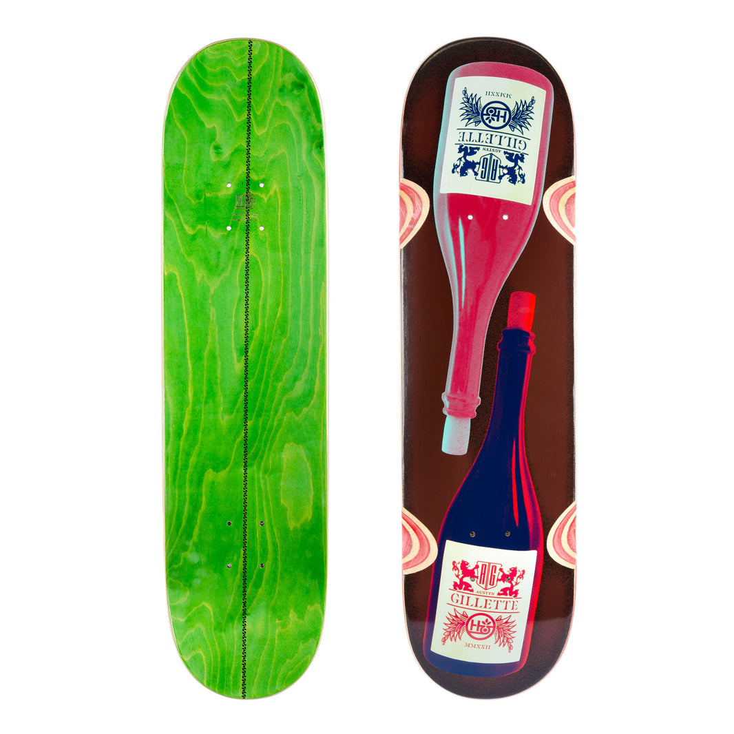 Habitat Austyn Bottleneck 8.25 skateboard deck: Dark brown deck with two wine bottles, one pink and one navy, lying head to tail with cream labels reading 'Gillette' and a crest. Pink slices appear at the edges. Green wood-stained underside shown alongside.