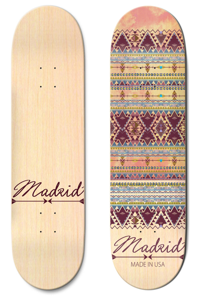Madrid Indie 8 skateboard deck: A band pattern of Aztec or tribal-style diamonds and zigzags in maroon, mustard, blue and pink over a sunset-pink sky on a natural maple deck. Madrid script logo with arrow at the bottom; the other deck shown is plain wood.