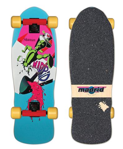 Madrid Shaman OG Cruiser skateboard deck: A retro 1980s-style scene of a green cartoon figure in a top hat crashing through a white shard shape, over a tipped black cup pouring pink liquid, with a Madrid logo, on pink and turquoise. Shown as a complete with yellow wheels and a grip-taped top.