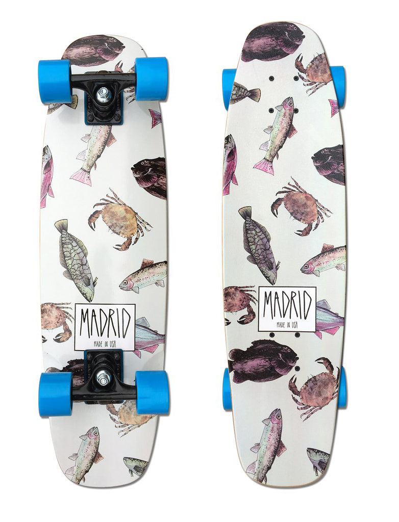 Madrid Squirt 29 skateboard deck: White cruiser with a scattered pattern of watercolour-style fish and crabs in pink, grey and brown. A boxed Madrid logo with 'Made in USA' sits near the bottom. Shown twice, with blue wheels.