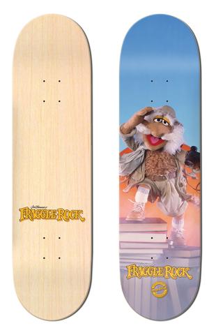 Madrid x Fraggle Rock Traveling Matt 8 skateboard deck: Traveling Matt, a shaggy Fraggle Rock puppet in an explorer's outfit, shades his eyes while standing on a stack of books against a blue and orange sky. Fraggle Rock logo at the bottom; the other deck is plain natural wood with a small logo.