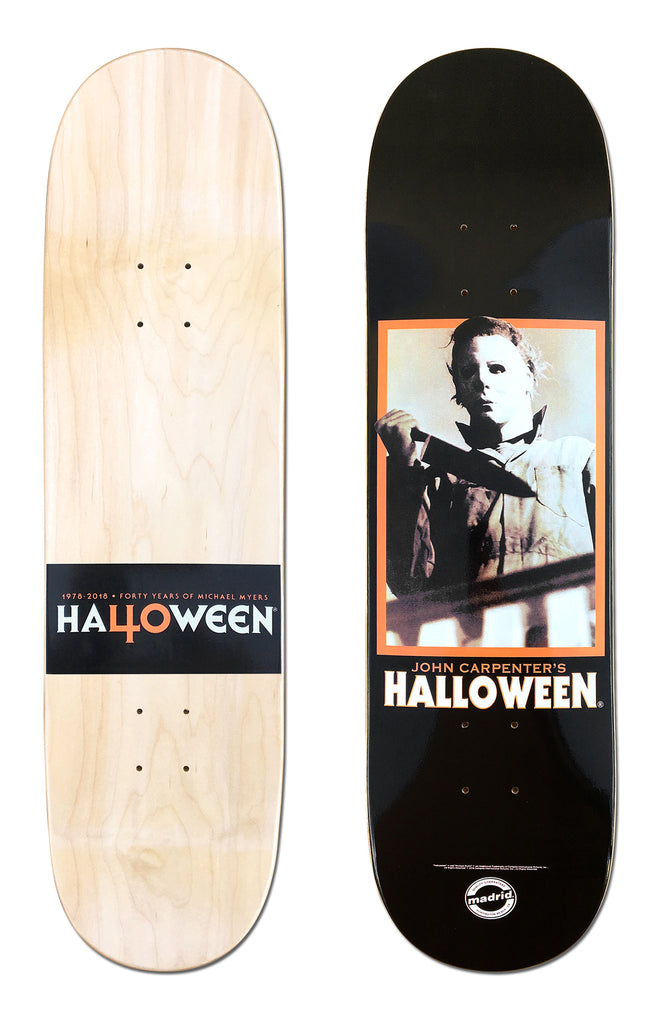Madrid X Halloween - Stalker 8 skateboard deck: Black deck with a framed film still of a masked figure in a boiler suit holding a knife, in an orange border, above 'John Carpenter's Halloween'. The natural wood underside has a black band reading 'Halloween' with a '40' for the O.