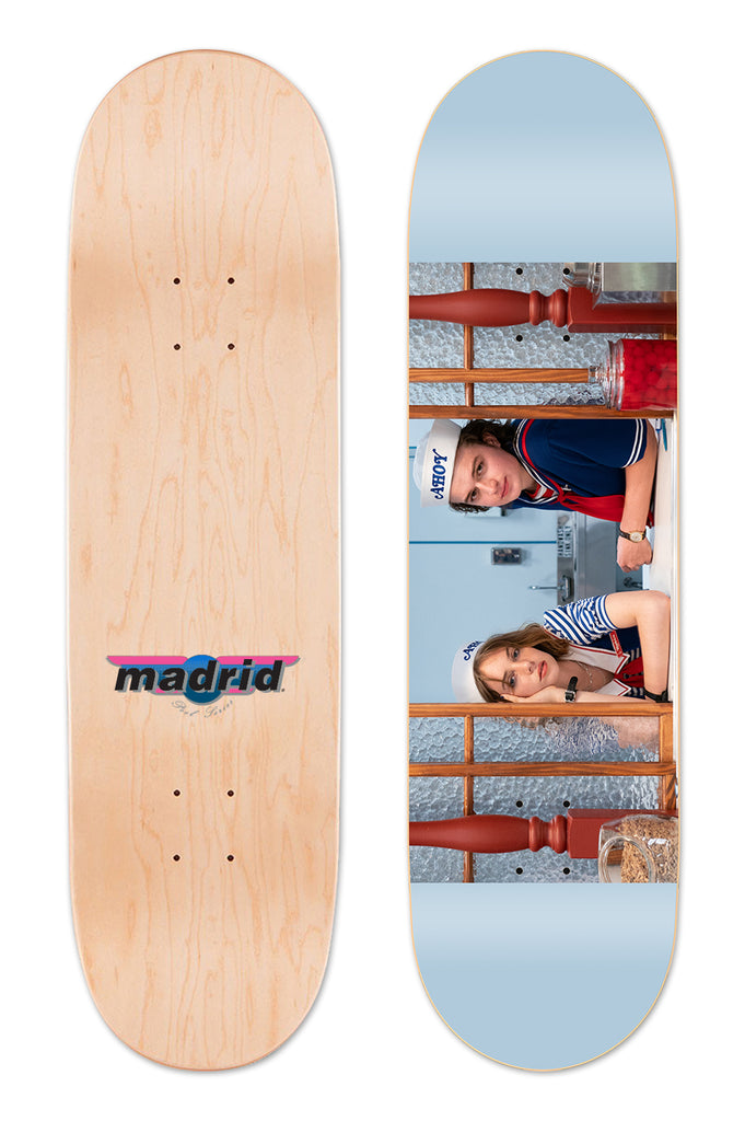 Madrid X Stranger Things 3 - Scoops Ahoy 8 skateboard deck: Photographic scene of two people in white sailor caps and navy and white striped uniforms leaning on a soda fountain counter with glass jars, set across a pale blue deck. The natural wood underside has a Madrid logo.