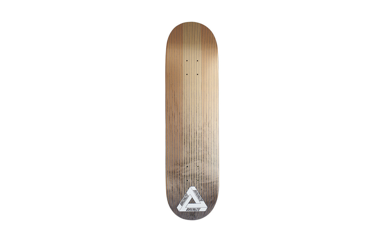 Palace Bronze Linear Board skateboard deck: Natural wood veneer with fine vertical pinstripes fading from bronze at the top to dark grey at the tail, with a white Palace triangle logo labelled BRONZE at the tail.