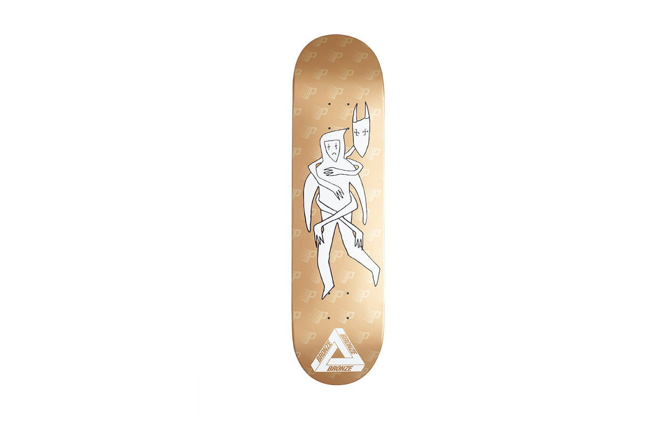 Palace Bronze Powers Board skateboard deck: A white line drawing of a figure embraced from behind by a long-armed creature with a pointed mask, on a gold deck with a faint repeating P pattern. A Palace tri-ferg style logo at the tail reads Bronze.