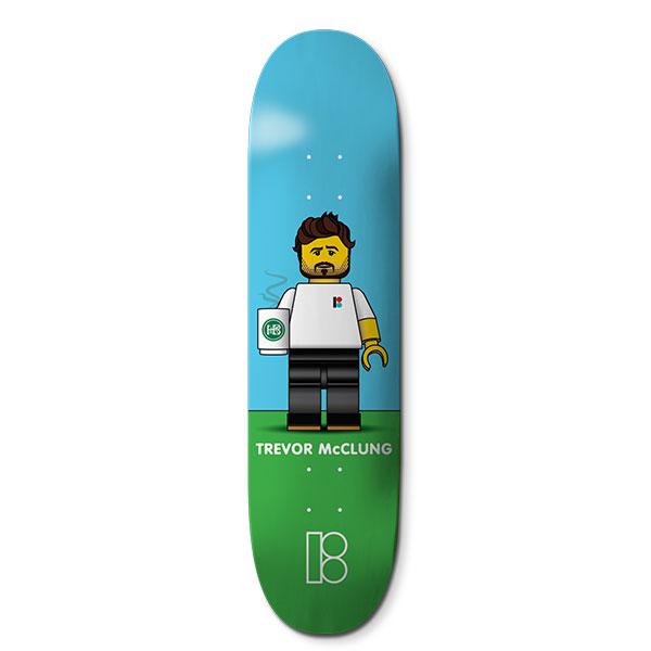 Plan B Trevor Blockhead - Pro skateboard deck: Toy-brick style minifigure of a bearded man with brown hair, in a white Plan B t-shirt and black trousers, holding a steaming coffee mug, standing on green grass against a blue sky. Name in white and Plan B logo at the tail.