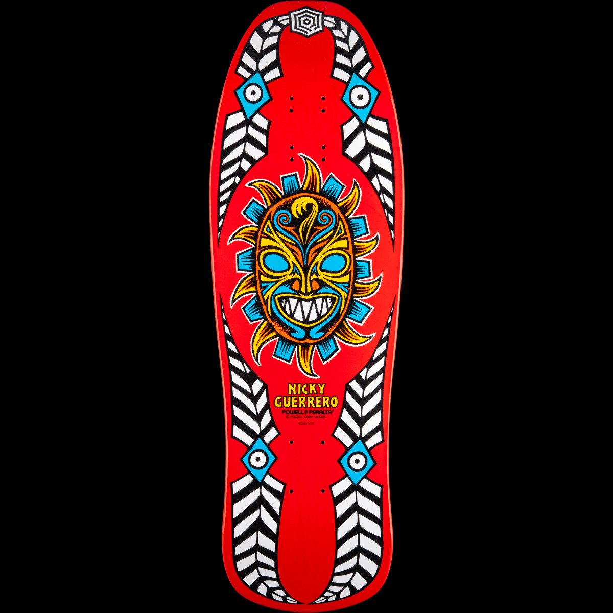 Powell Peralta Guerrero Mask Blem Natural skateboard deck: Tribal sun mask with a toothy grin and blue eyes in a yellow and blue sunburst, framed by black and white feather-pattern borders with blue eye motifs, on red.