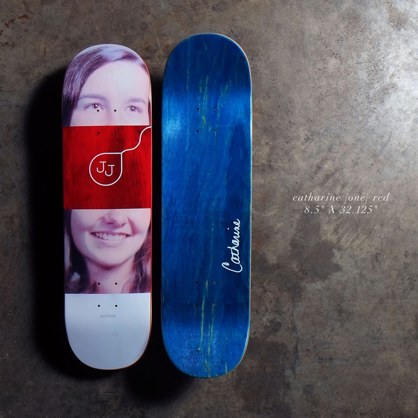 Quasi Catharine - Red skateboard deck: A photographic portrait of a smiling young woman with long hair, split by a red band with a JJ monogram and a looped line. The bottom side is shown in blue stain with a white signature.