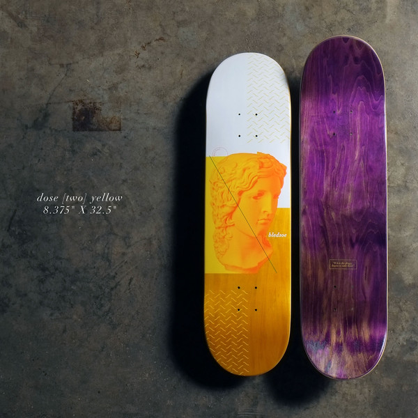 Quasi Dose - Yellow skateboard deck: White and yellow deck with an orange-toned classical marble bust, a diagonal line across it and zig-zag line patterns. Rider name beside the bust; purple stained underside shown alongside.