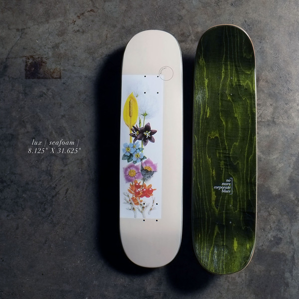 Quasi Lux8.125 - Crème skateboard deck: A cream deck with a white panel of botanical flower illustrations in yellow, purple, blue, pink and orange, stacked up the centre, with a small circle logo above. The underside is dark green stained wood with small text.