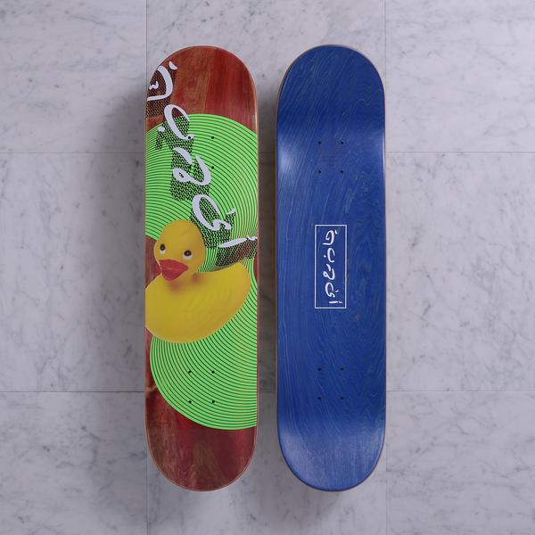 Quasi Ducking Red skateboard deck: Yellow rubber duck photographed in front of a green circle of concentric lines, with white Arabic-style script lettering running down a red stained deck. Underside is blue with a boxed script logo.