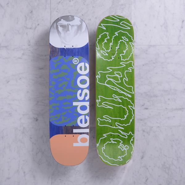 Quasi Metalhead Peach skateboard deck: Two views shown. One has a grey face portrait at the top, a blue panel with camouflage-like green pattern and large white vertical 'bledsoe' text, and a peach block at the base. The other is a green deck with a white wobbly outline of 'Quasi' lettering.