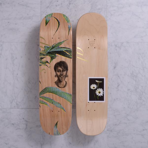 Quasi Mother Natural skateboard deck: Two sides shown on natural wood. One has a pencil-style portrait of a smiling woman among green halftone leaves with gold lettering. The other has a small framed photograph of white daisies on a black background.