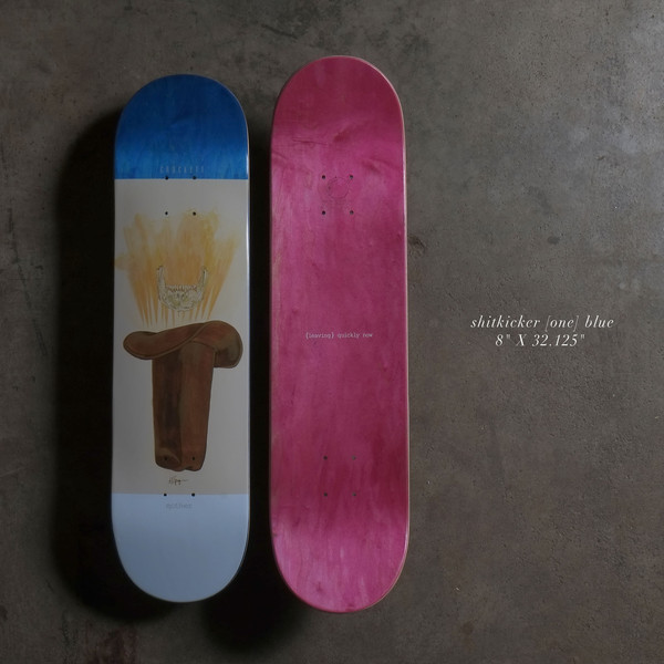 Quasi Shitkicker 8 - Blue skateboard deck: Painted brown cowboy saddle with a glowing yellow animal skull above it, on a cream panel between a blue top and pale blue base. A second deck shows a plain pink stained underside with small text.